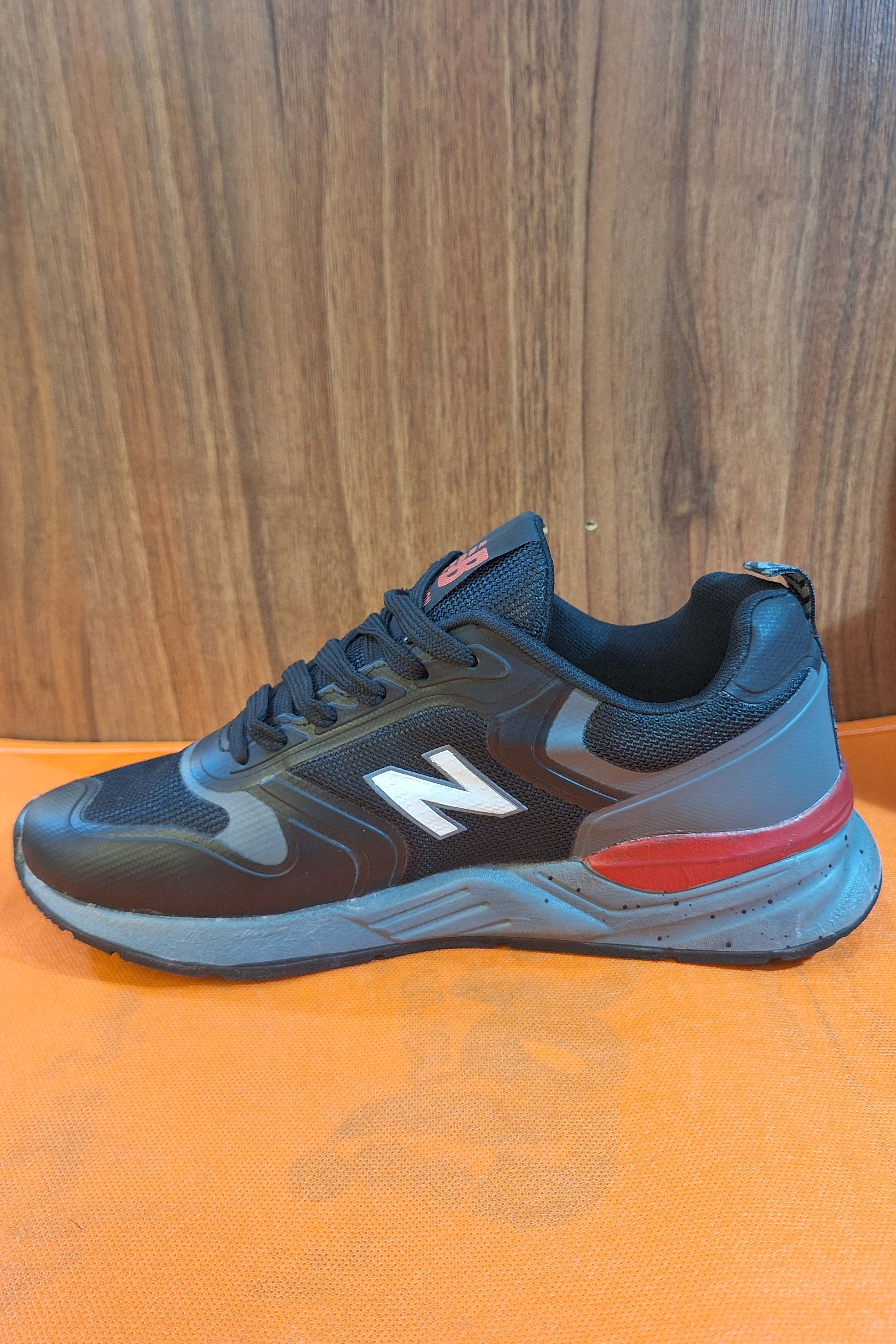 کتانی رانینگ (Running) مردانه طرح نیوبالانس (New Balance) مشکی با لوگوی N سفید و زیره آجدار خاکستری/قرمز، کفش اسپرت روزمره شیک